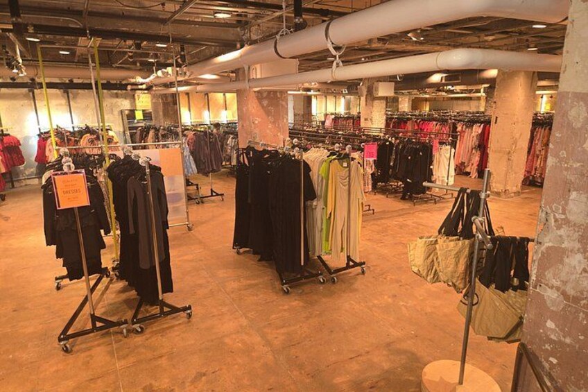Un magasin de vêtements avec des portants remplis de vêtements et une enseigne indiquant une période de soldes. 2
