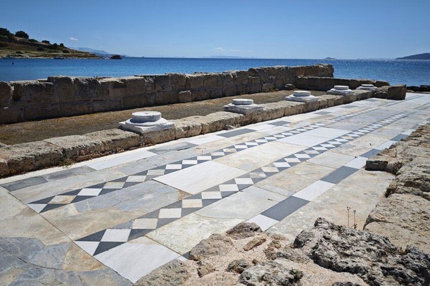 A historical stone pathway with geometric patterns, leading to a coastal area with ruins and a view of the sea. 3