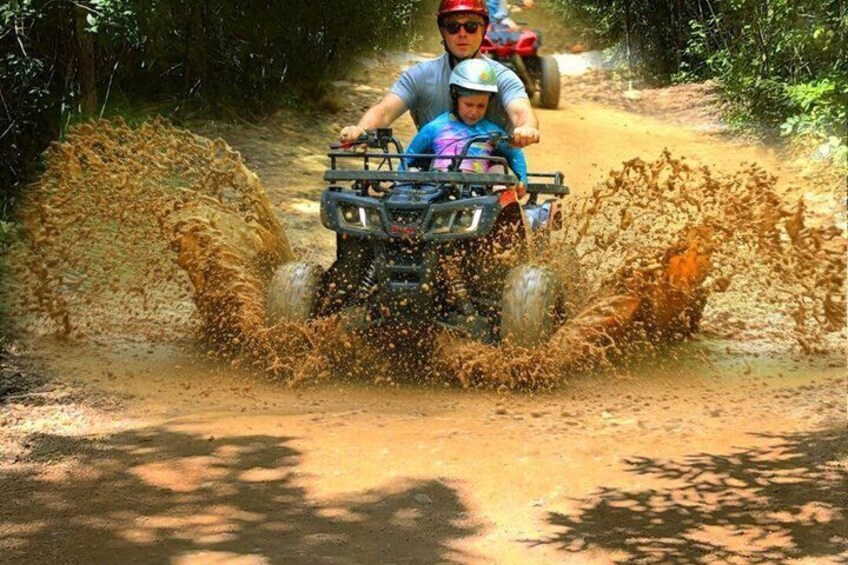 A person driving an ATV through a muddy area, splashing mud around. 5