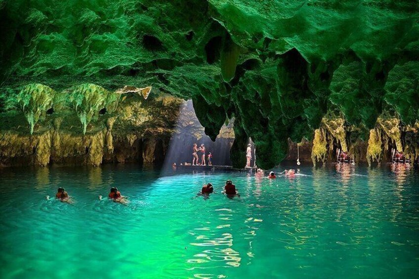 A cave with turquoise water and people swimming. 3