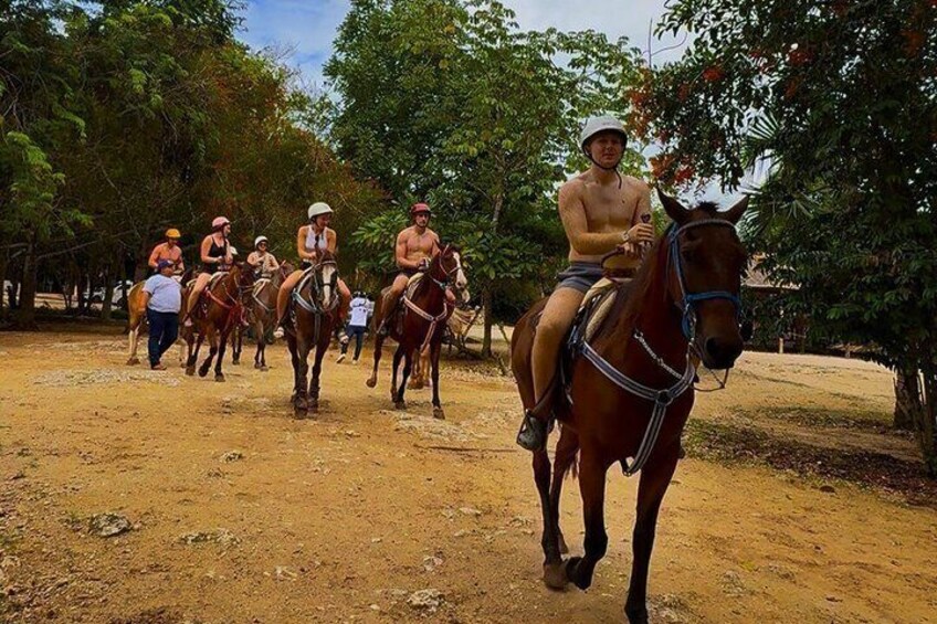 A group of people riding horses on a dirt path surrounded by trees. 4