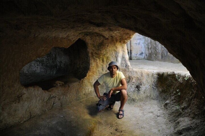 A person crouching inside a cave with a large rock formation to the left. 5