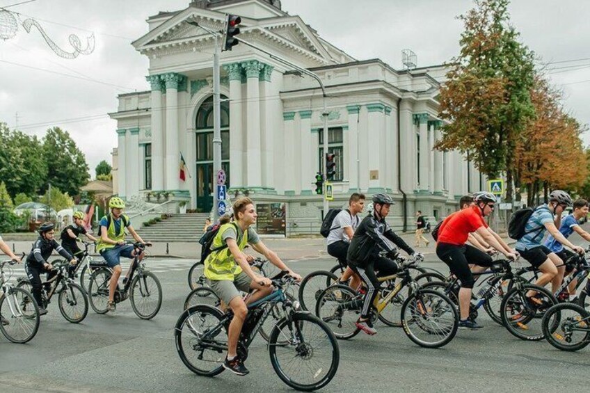 A group of cyclists riding on a street with a classical building in the background. 1