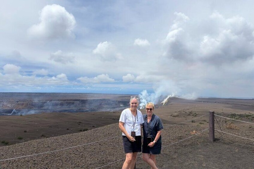 Two people standing on a gravel path with a barren landscape and a plume of smoke in the distance. 5