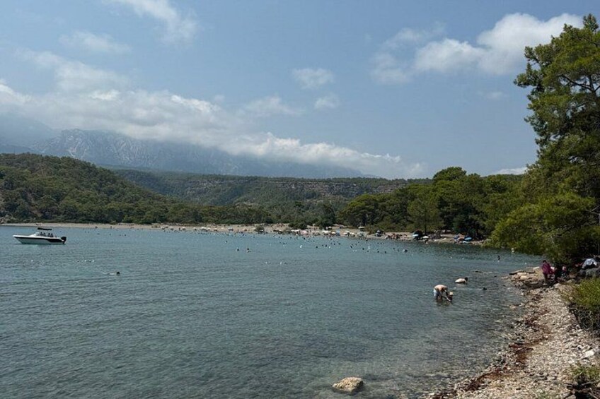 A lake with boats, people swimming, and a forested hillside. 1