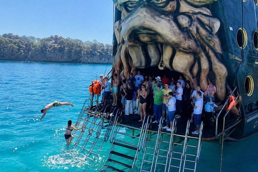 A large ship with a mural of a face, people swimming in the water, and a crowd on the ship's deck. 5
