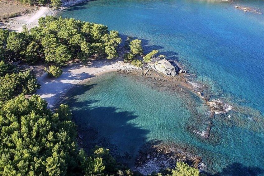 A coastal landscape with clear blue waters, sandy beach, and dense green trees. 5