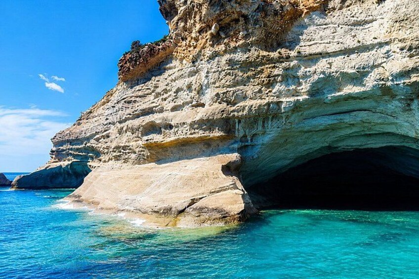 A coastal cliff with a cave entrance, clear turquoise water, and a rocky shoreline. 3