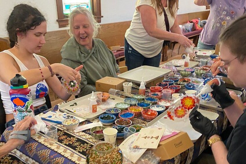 A group of people engaged in a craft activity with various colorful materials and bowls on a table. 3