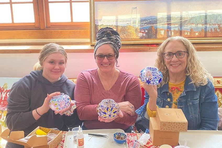 Three people holding decorated glass balls at a table with various items. 1