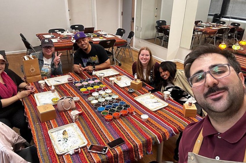 A group of people seated around a table with various items, including a tray of colorful objects and a smartphone. 2
