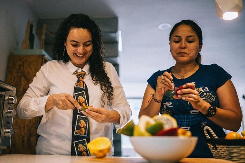 Two people preparing food, one wearing a white shirt and tie, the other in a blue shirt, with a bowl of fruit on the counter. 4