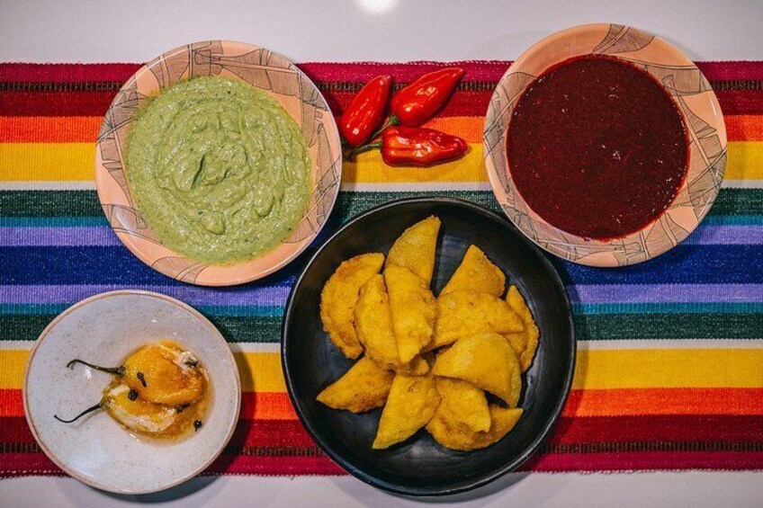A plate of yellow fritters, a bowl of green sauce, and a bowl of red sauce on a colorful striped tablecloth. 1