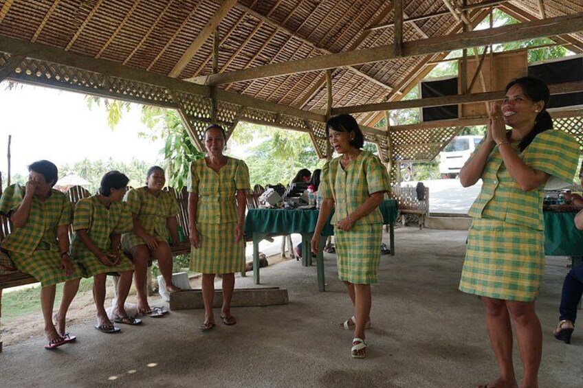 A group of people in matching checkered dresses standing in a covered outdoor area with tables and chairs. 4