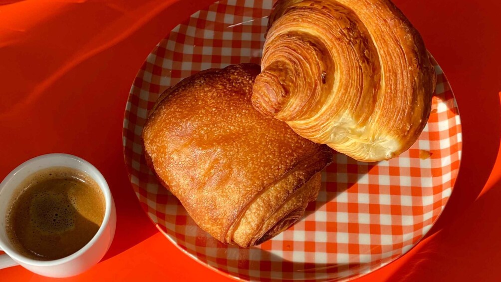 A croissant and a cup of coffee on a checkered plate. 1