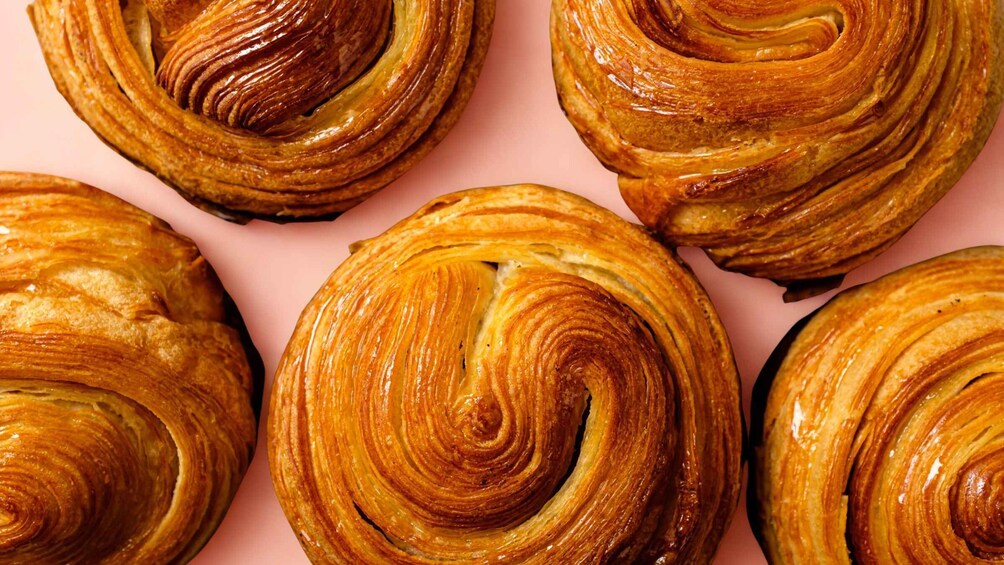 A group of golden-brown pastries with a spiral design on a pink background. 3