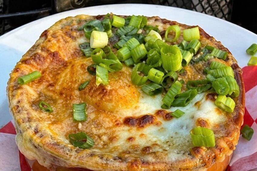 A round, golden-brown dish topped with melted cheese and chopped green onions. 1