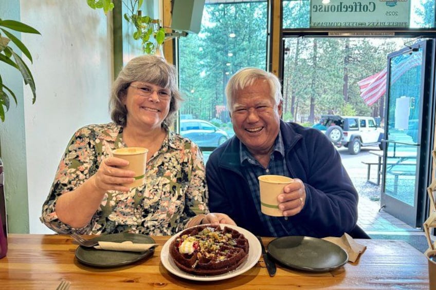 Two people sitting at a table with a cake and coffee cups. 4