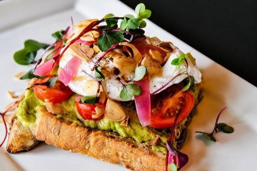 A sandwich with avocado, tomato, and greens on a slice of bread. 2