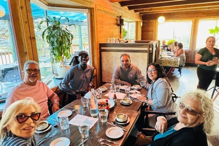 A group of people dining at a wooden table in a restaurant with large windows. 1