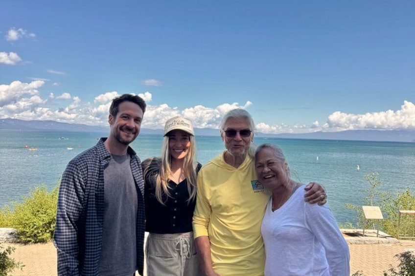 A group of people standing by a body of water with a clear sky and distant mountains. 1