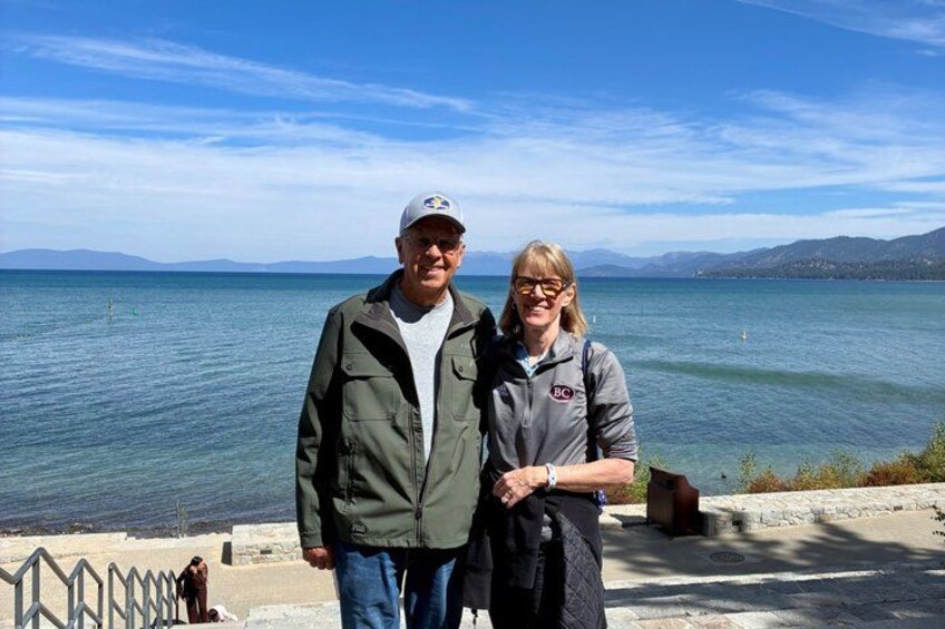 Two people standing by a waterfront with a clear sky and distant mountains. 3