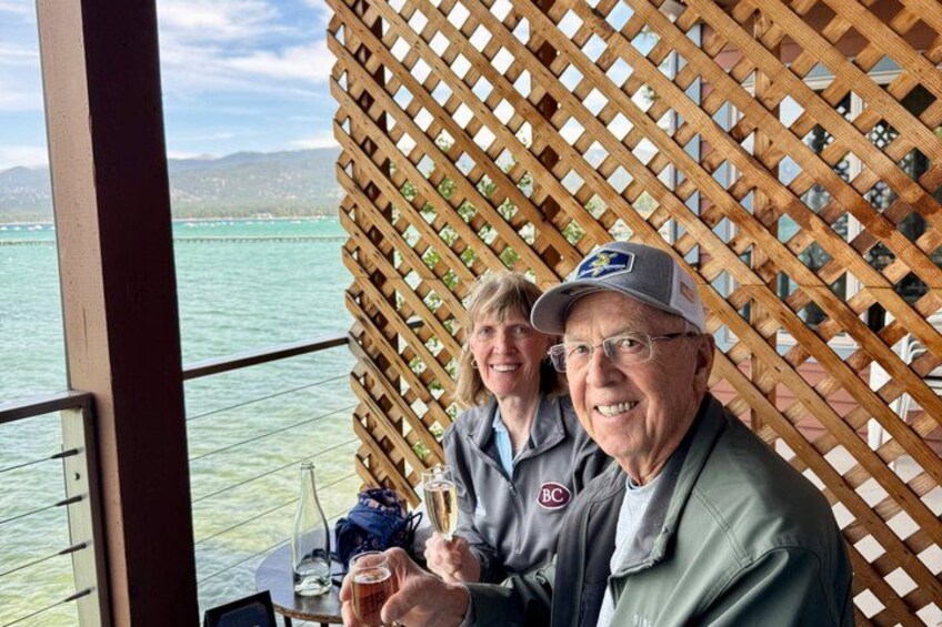 A person sitting at a table with a drink and a glass, a wooden lattice wall, and a view of the sea. 2