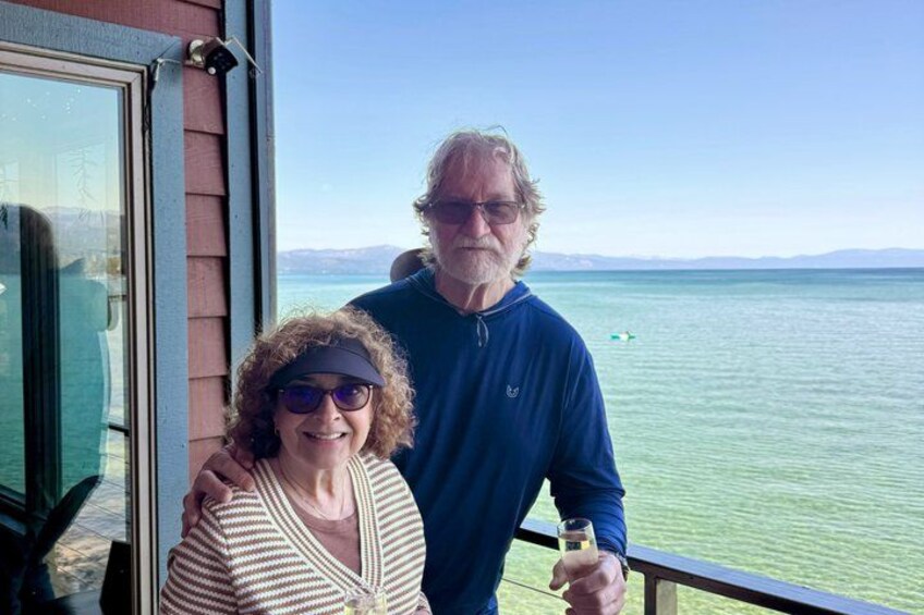 Two people standing by a window overlooking a body of water with mountains in the distance. 4