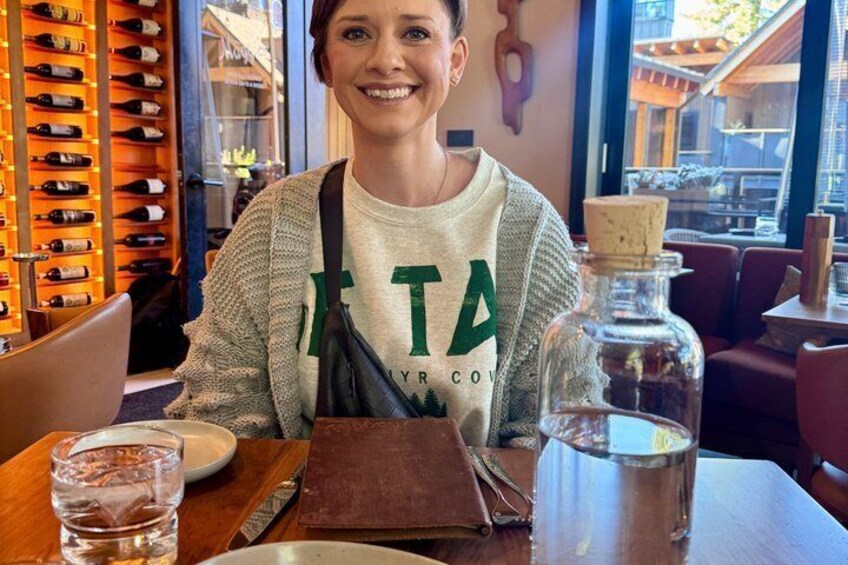 A person seated at a table with a bottle of water, a glass, and a menu. 3
