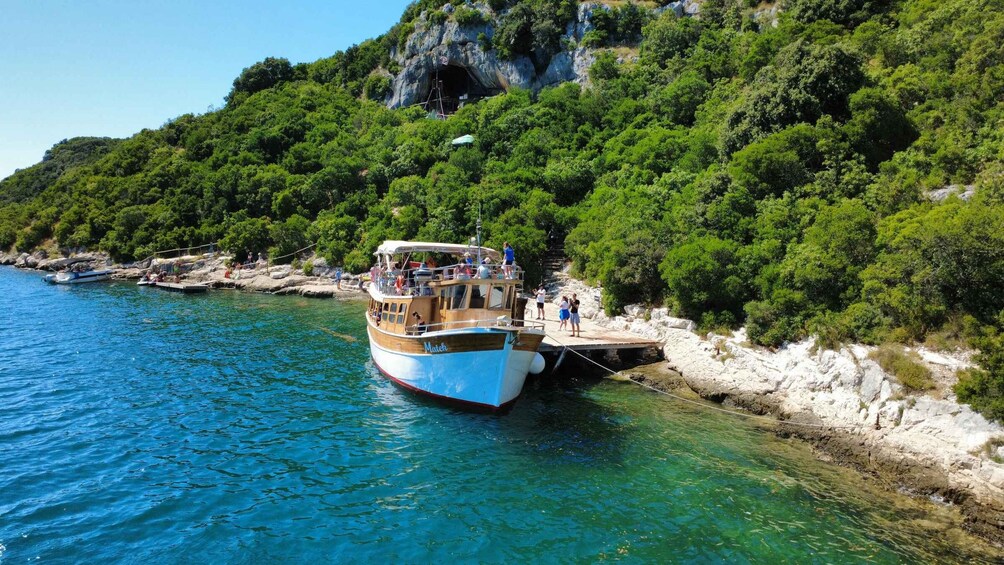 A boat docked at a rocky shore with lush greenery and a clear blue sea. 2