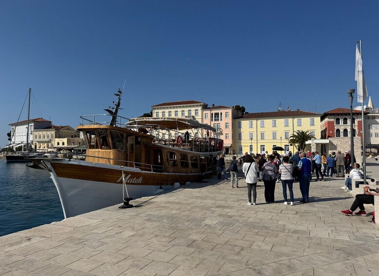 A wooden boat docked at a waterfront promenade with people walking and a historic building in the background. 3