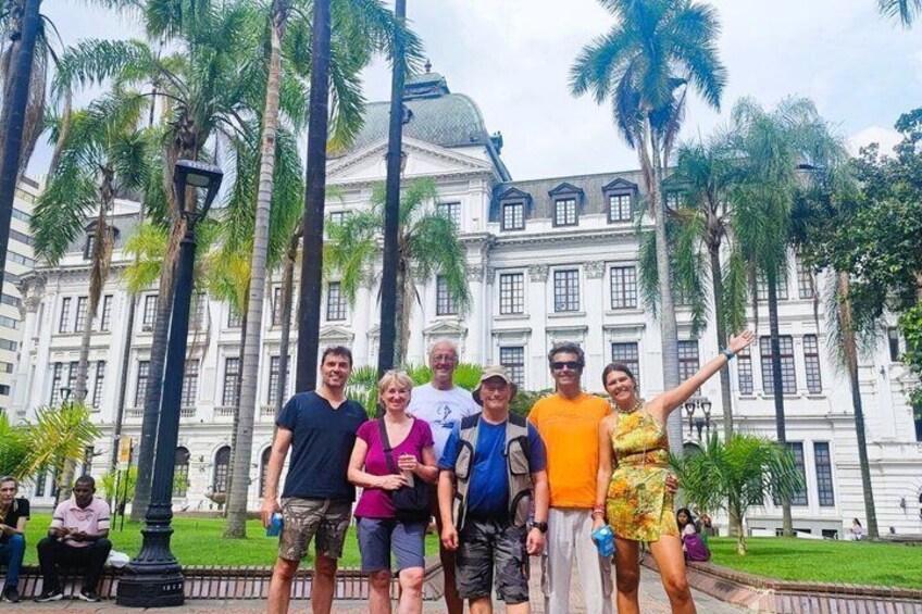 A group of people standing in front of a large white building with columns and palm trees. 5