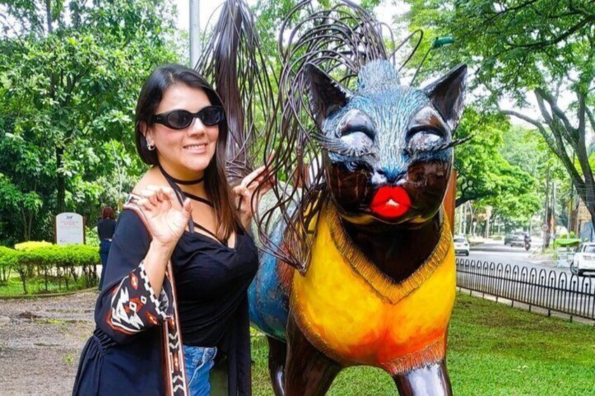 A person standing next to a colorful cat statue in a park. 4