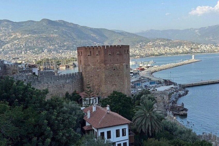 A coastal cityscape with a prominent castle tower, a marina, and a mountainous backdrop. 2