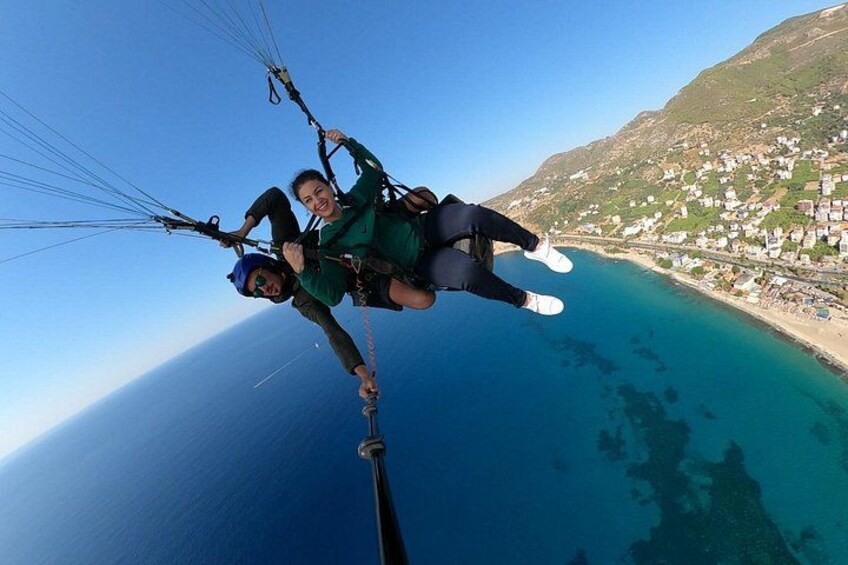 Two people paragliding over a coastal area with clear blue waters and a hilly landscape in the background. 5