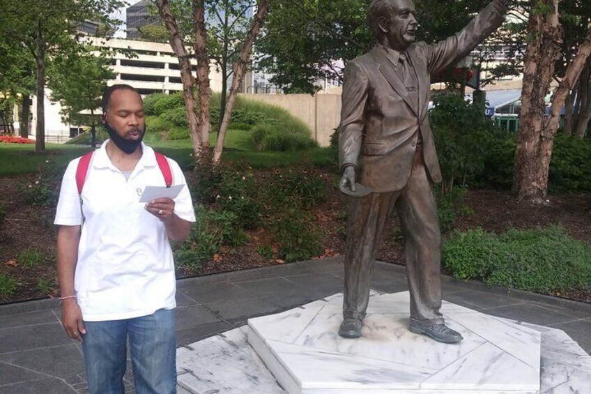 A person standing next to a bronze statue of a man in a suit with one arm raised. 2