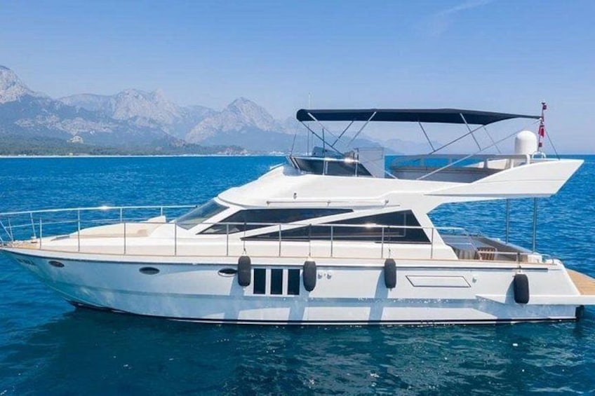 A white yacht with a covered deck, anchored in clear blue waters with mountains in the background. 4