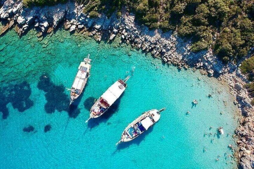 Three boats anchored in clear turquoise waters with rocky coastline and dense greenery. 2