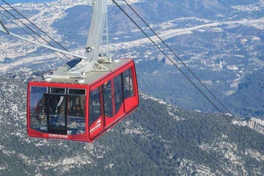 A red cable car suspended by cables, high above a mountainous landscape with snow-covered peaks. 3