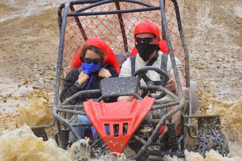 Two people in a vehicle with a red canopy, driving through a muddy terrain. 3