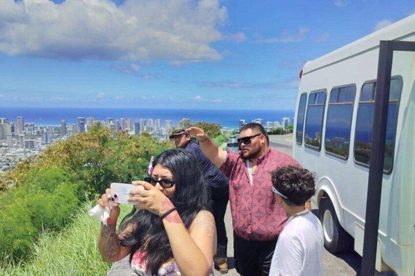 A group of people taking photos with a cityscape and ocean in the background. 3