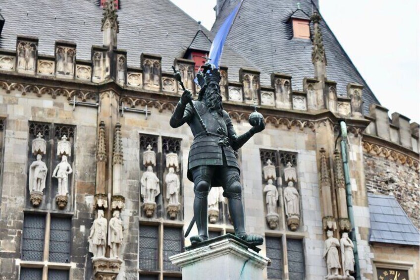 A statue of a knight in armor on a pedestal in front of a building with Gothic architecture and multiple statues. 3