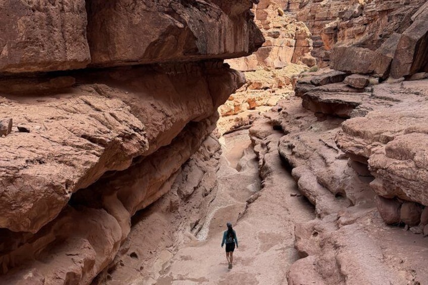 A person walking through a narrow canyon with layered rock formations. 2