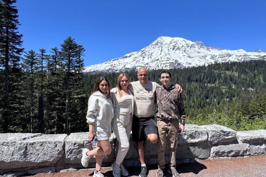 A group of people posing in front of a snow-capped mountain with a forested background. 2