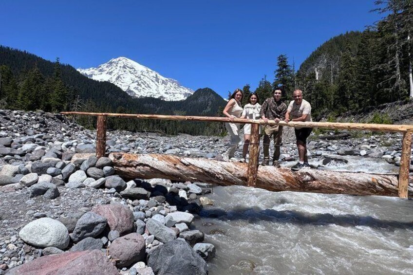 A group of people standing on a wooden bridge over a river with a snow-capped mountain in the background. 4