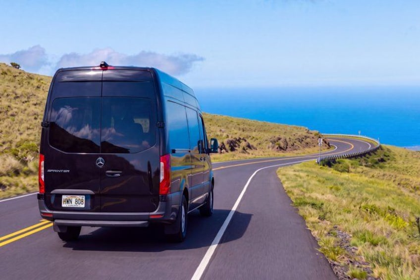 A black van driving on a winding road with a coastal view. 3