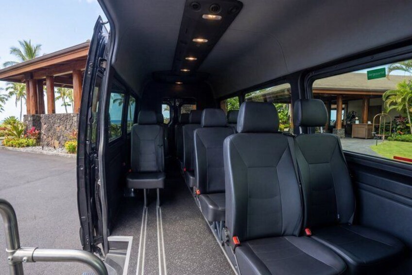 A vehicle interior with black seats and a door open to a parking area. 4