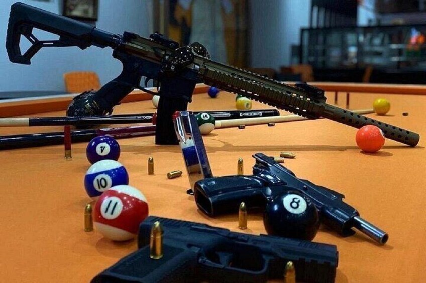 A pool table with billiard balls, cue sticks, and firearms. 5