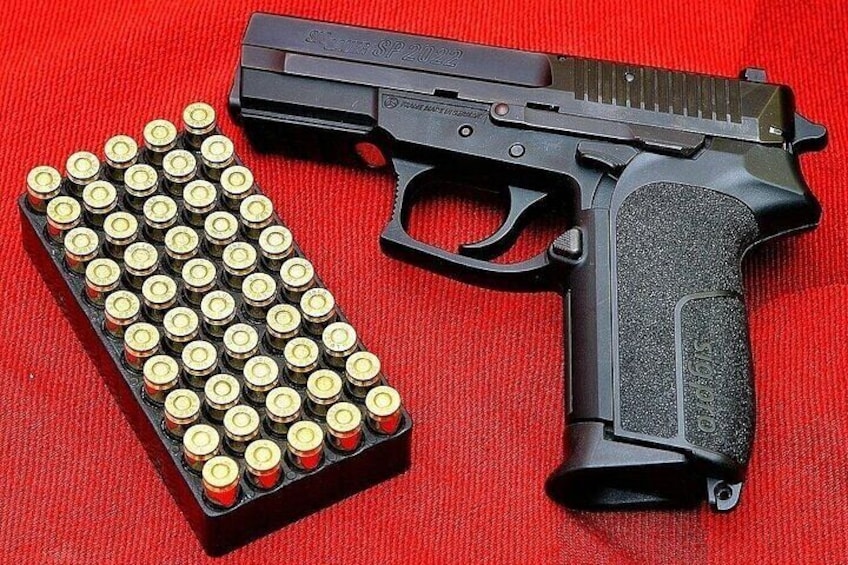 A handgun and a magazine with bullets on a red fabric background. 1