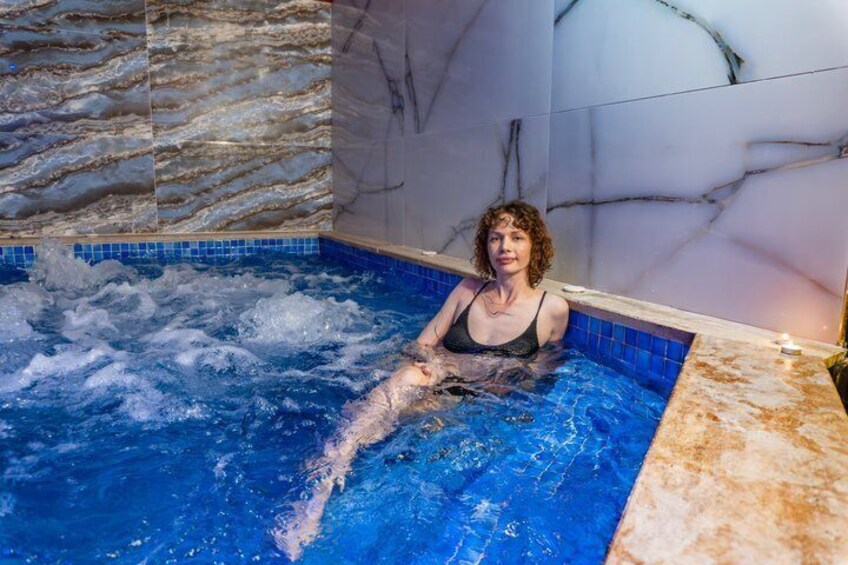 A person in a hot tub with blue tiles and marble walls. 3